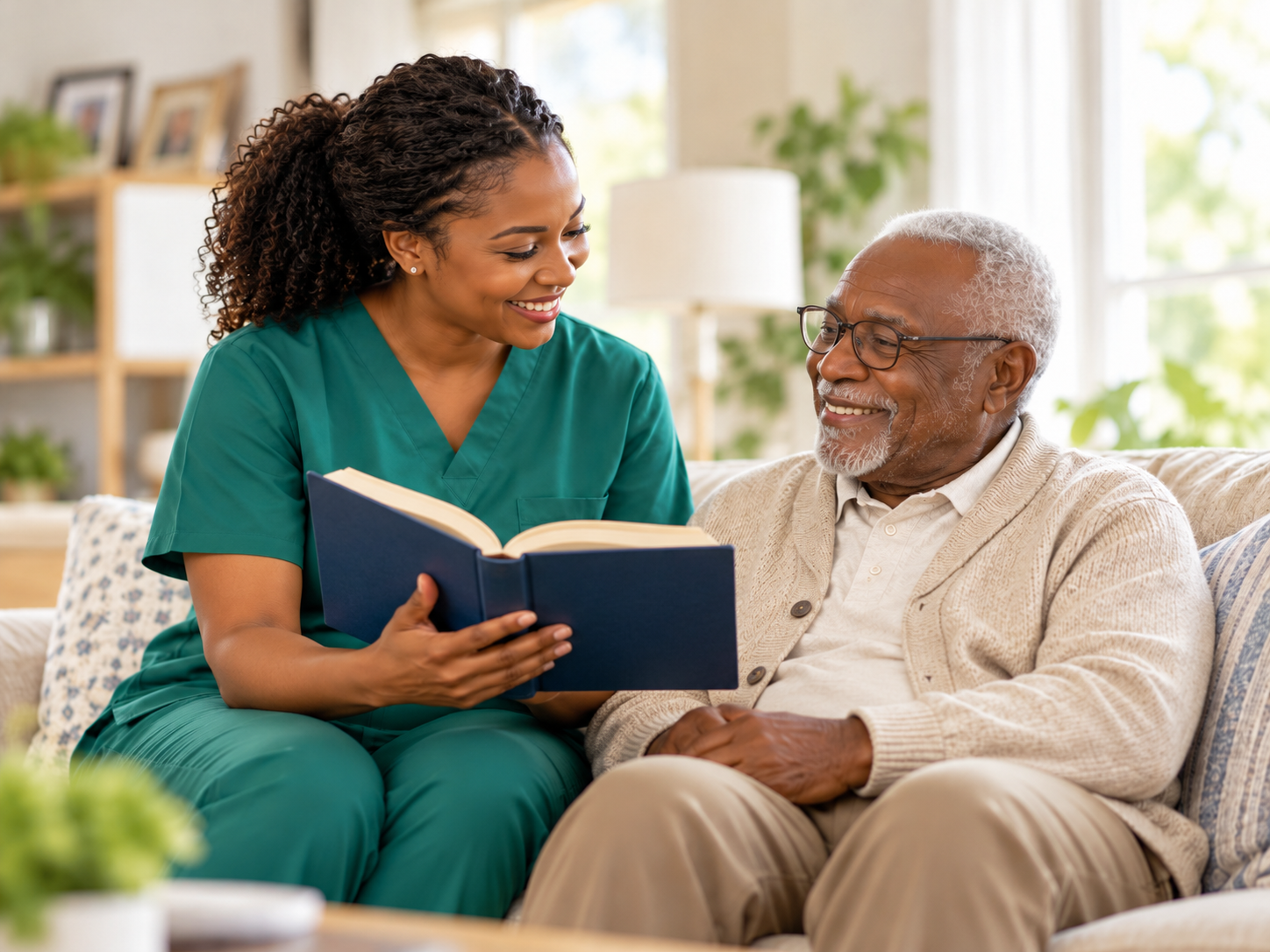 Black female caregiver in green scrubs reading a book with an older gentleman at home